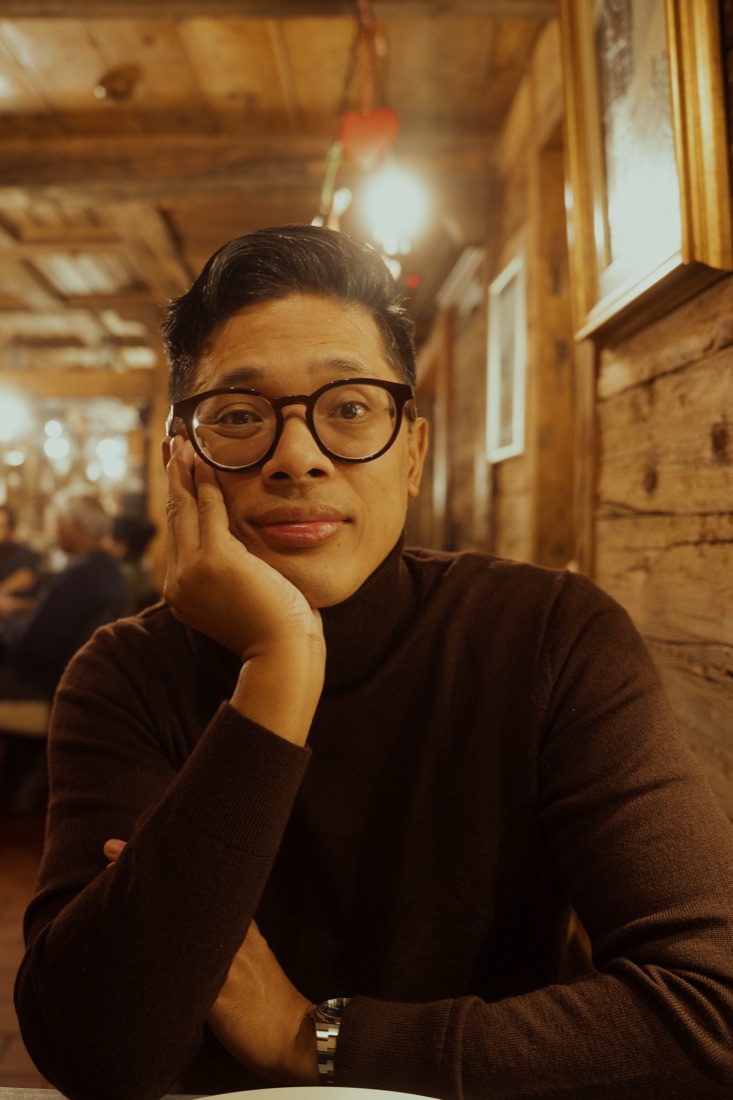 George at a table in a wooden alpine restaurant, chin resting on one hand